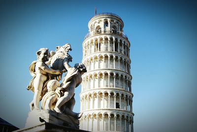 Statue by leaning tower of pisa against clear blue sky