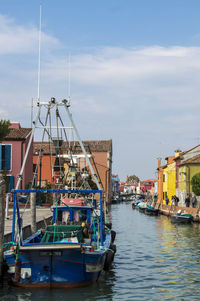 Boats moored at harbor in city against sky