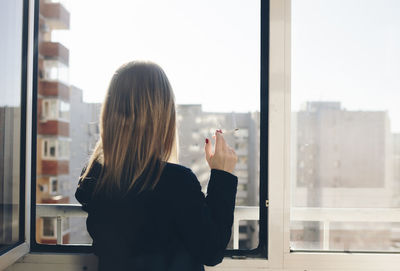 Rear view of woman smoking cigarette by window