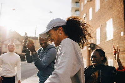 Man holding speaker while friends dancing in city on sunny day