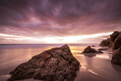 Rock formation in sea against sky during sunset