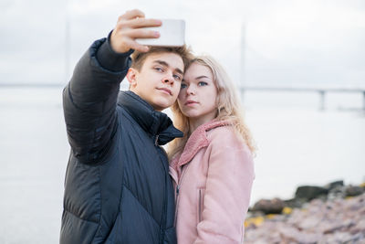 Couple taking selfie while standing against sea