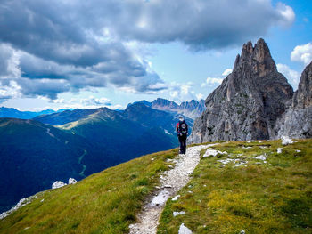 Rear view of male hiker standing on mountain against cloudy sky