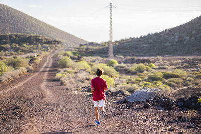 Rear view of man walking on road against mountain