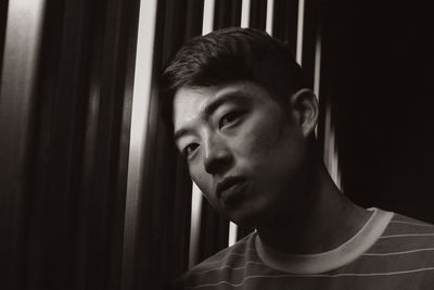 Portrait of young man by blinds at home