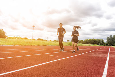 People running on sports track against cloudy sky