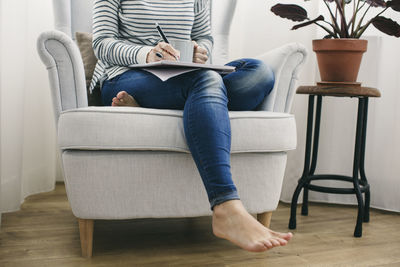 Woman sitting in armchair writing on notepad