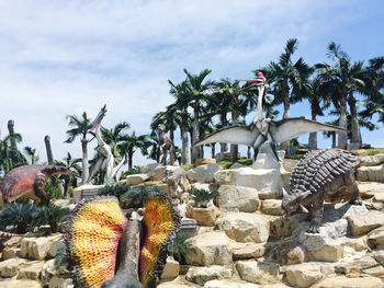 Statue by palm trees and rocks against sky