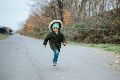 Full length portrait of smiling boy running on road