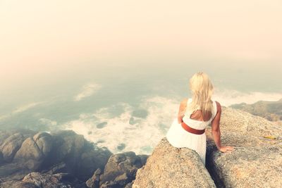 Woman sitting on rock against sky