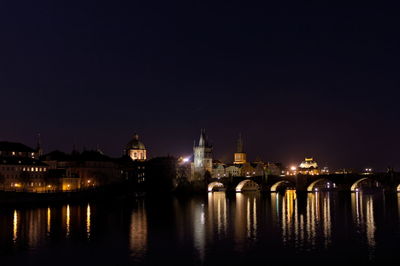 Illuminated buildings by river against sky at night