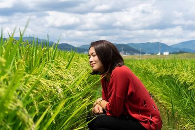 Side view of woman sitting on field against sky