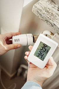 Woman adjusting radiator temperature and holding thermostat