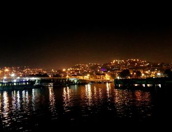 Illuminated cityscape by river against sky at night