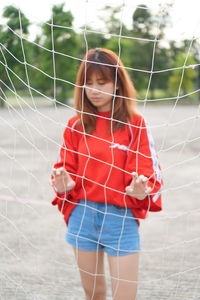 Young woman standing by net on land