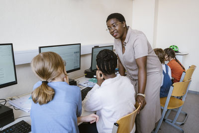Female teacher talking with children sitting in computer class at school