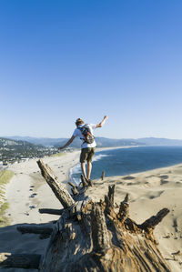 Rear view of man with backpack walking on sand at beach against clear blue sky