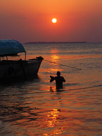 Silhouette man standing in sea against orange sky during sunset