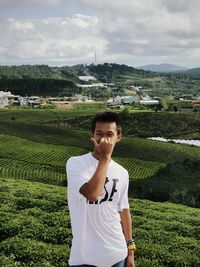 Portrait of teenage boy standing on field against sky