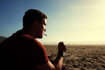 Side view of man smoking cigarette while sitting at beach