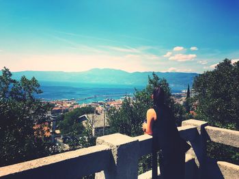 Rear view of woman at terrace against sky on sunny day