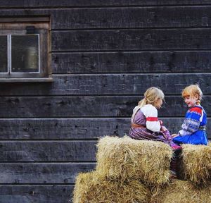 Full length of happy woman sitting on barn