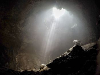 Low angle view of sunlight streaming through rocks against sky