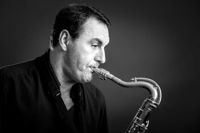Close-up of man playing brass instrument against gray background