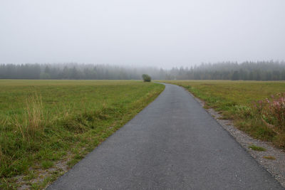 Road amidst field against sky during foggy weather