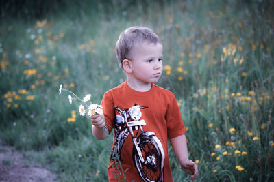 Full length of cute boy holding camera on field