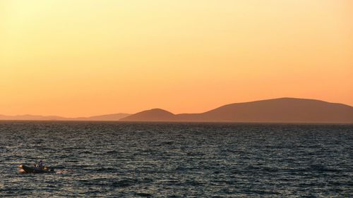 Full frame shot of orange sunset in coastal mountain landscape with small boat on sea