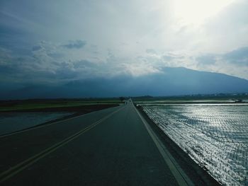 Empty road amidst field against sky