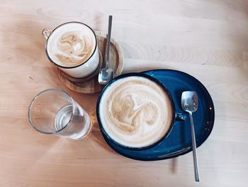 Flatlay with two blue coffee cups with latte and cappuccino, spoons, glass of water