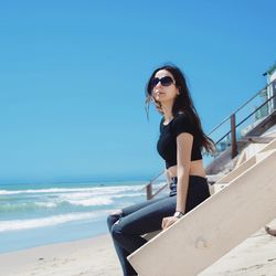 Portrait of smiling young woman on beach against clear blue sky