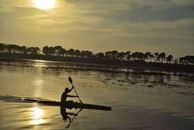 Man kayaking at lake against sky during sunset