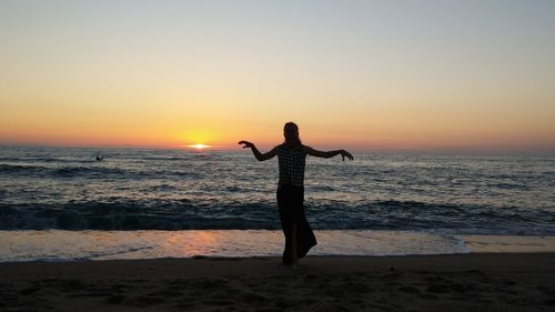 Rear view of person standing on beach during sunset