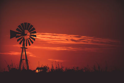 Silhouette american-style windmill on field against red sky during sunset