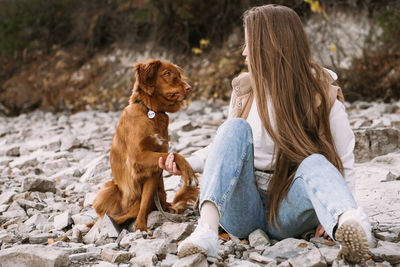 Young woman and dog retriever walks on river shore at autumn season