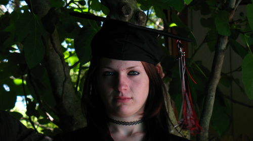 Portrait of young woman wearing mortarboard against plants