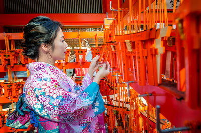 Young woman in traditional clothing looking at prayer label in shrine