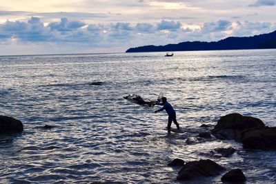 Silhouette man standing on sea against sky during sunset