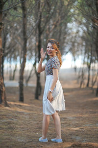 Woman smiling and waving hand with dry branches background