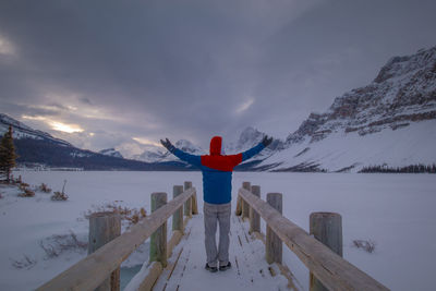 Rear view of man standing against snowcapped mountain during dawn