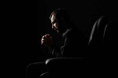 Worried man sitting on armchair in darkroom