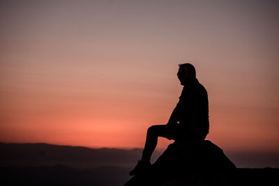 Silhouette man sitting on rock against sky during sunset