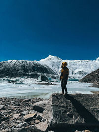 Rear view of person standing on snowcapped mountain against blue sky