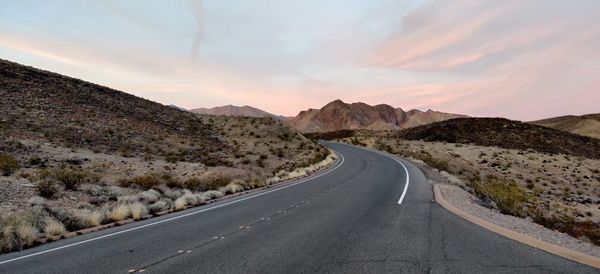 Empty road leading towards mountains against sky