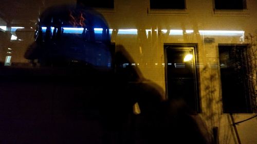 Reflection of woman on illuminated building at night