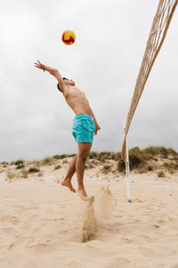 Full length of shirtless man playing volleyball at beach