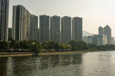 Modern buildings by river against sky in city